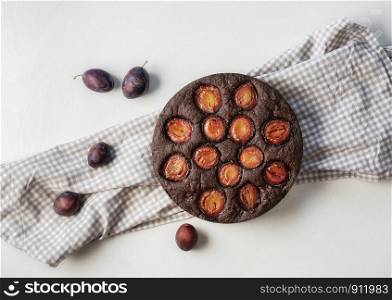 Fruitcake with plums and cocoa on a kitchen towel and white tabletop. Above view of autumn dessert. Flat lay of plum pie. Tasty fruit tart.