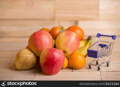 fruits and a shopping cart on a wooden table, studio picture