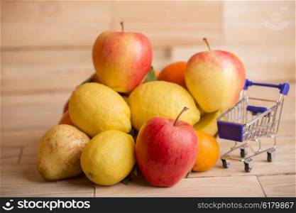 fruits and a shopping cart on a wooden table, studio picture