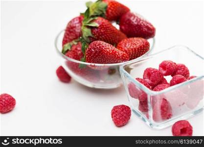 fruits, berries, diet, eco food and objects concept - close up of juicy fresh ripe red strawberries and raspberries in glass bowls over white