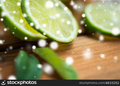 fruits, citrus, detox, diet and objects concept - close up of lime slices on wooden table over snow