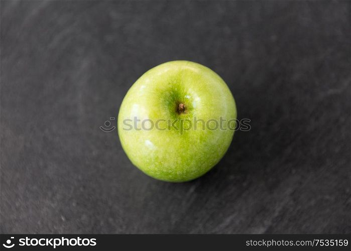 fruits, diet, eco food and objects concept - ripe green apple on slate stone background. ripe green apple on slate stone background