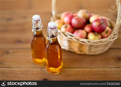 fruits, food and harvest concept - apples in wicker basket and glass bottles of juice on wooden table. apples in basket and bottles of juice on table