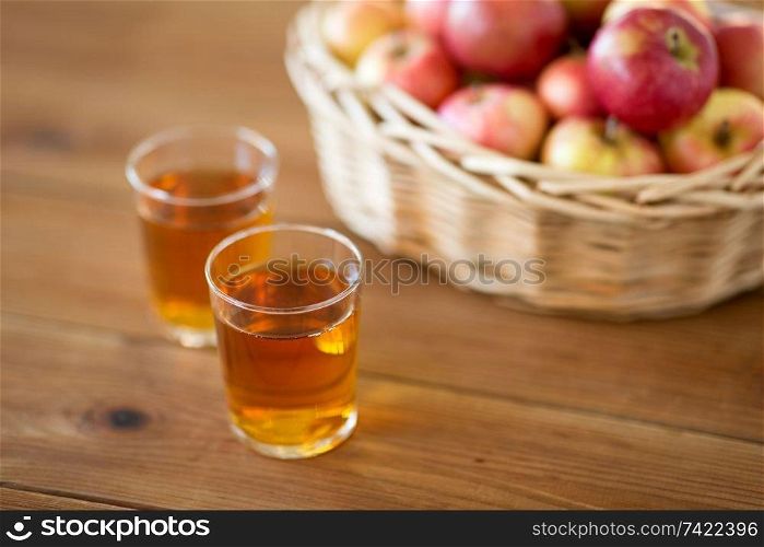 fruits, food and harvest concept - apples in wicker basket and glasses of juice on wooden table. apples in basket and glasses of juice on table