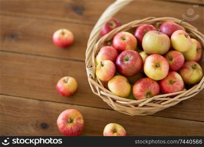 fruits, food and harvest concept - ripe apples in wicker basket on wooden table. ripe apples in wicker basket on wooden table