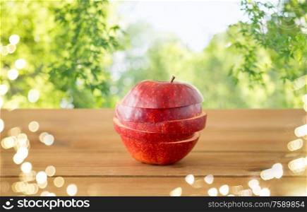 fruits, food and harvest concept - sliced red apple on wooden table over green natural background. sliced red apple on wooden table