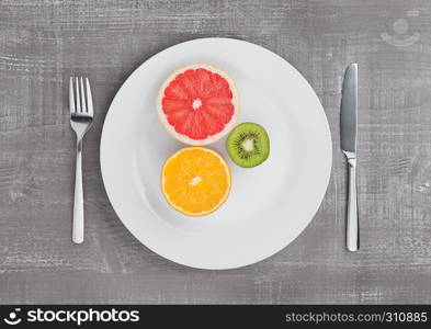 Fruits mix grapefruit orange and kiwi on the plate on wooden background