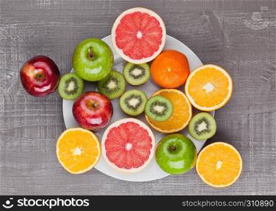 Fruits mix grapefruit orange and kiwi on the plate on wooden background