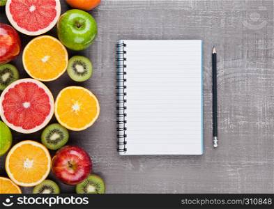 Fruits mix grapefruit orange apples with notebook on wooden background