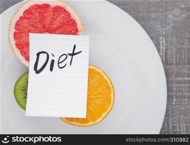 Fruits mix grapefruit orange kiwi on plate with diet sign on wooden board