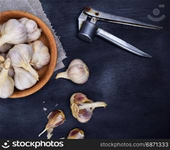 Fruits of garlic in a wooden bowl and on a black table, top view