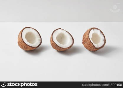 Fruits pattern from three exotic organic natural halves of ripe coconuts on a duotone light grey background with soft shadows, copy space. Vegetarian concept.. Set from three tropical natural halves of coconut on a light grey background.