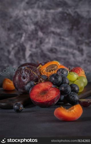 Fruits Still life with fruit on whte ceramic bowl. Concrete wall. Dramatic light. Grapes, apricots and plums.