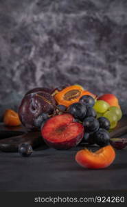 Fruits Still life with fruit on whte ceramic bowl. Concrete wall. Dramatic light. Grapes, apricots and plums.