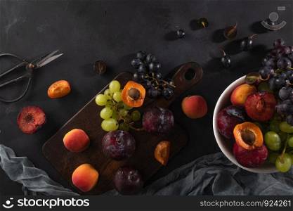 Fruits Still life with fruit on whte ceramic bowl. Concrete wall. Dramatic light. Grapes, apricots and plums.
