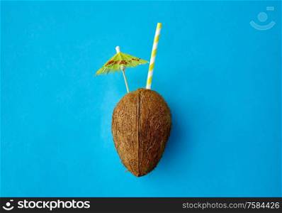 fruits, summer and food concept - coconut drink with paper straw and cocktail umbrella on blue background. coconut drink with straw and cocktail umbrella