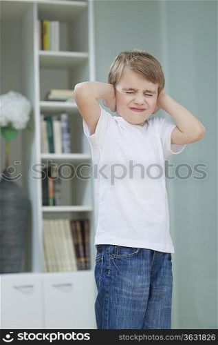 Frustrated boy covering his ears with hands at home