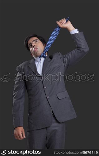Frustrated businessman hanging himself with tie against black background