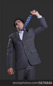 Frustrated businessman hanging himself with tie against black background
