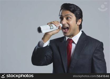 Frustrated businessman shouting through newspaper against gray background