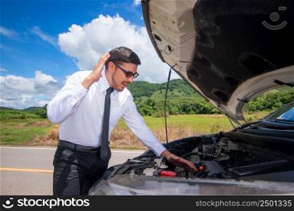 Frustrated businessman with his broken car looking in frustration at failed engine.