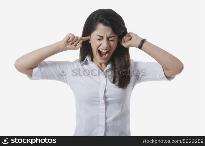 Frustrated businesswoman with fingers in ears yelling against white background