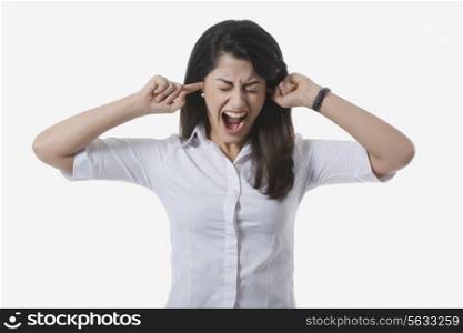 Frustrated businesswoman with fingers in ears yelling against white background