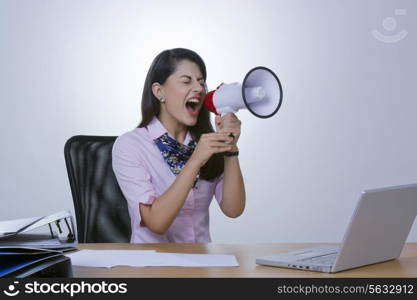 Frustrated businesswoman yelling in megaphone at office desk