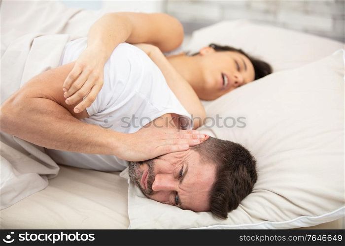 frustrated man covers ears with pillow cannot fall asleep
