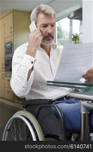 Frustrated Man In Wheelchair Making Phone Call Whilst Reading Letter