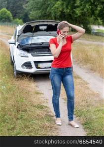 Frustrated woman calling for help with her broken car at rural road