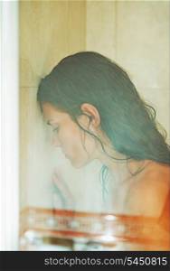 Frustrated woman leaning on weeping glass shower door