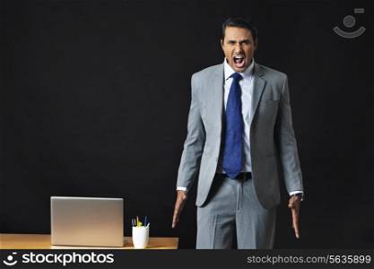Frustrated young businessman screaming by office desk