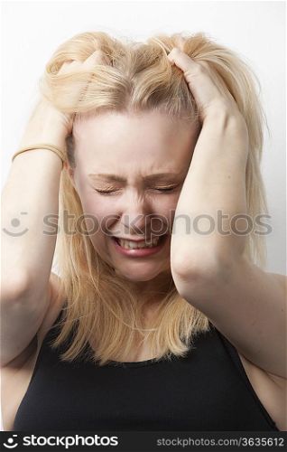 Frustrated young Caucasian woman with hands in hair against white background
