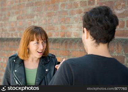 Frustrated young couple having argument and quarrelling with each other outdoors in the street. Relationship problems.