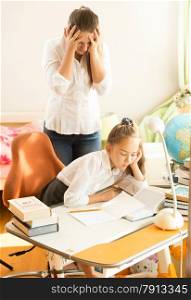 Frustrated young mother looking daughter sleeping while doing homework