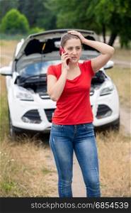 Frustrated young woman calling for help with her broken car