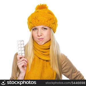 Frustrated young woman in hat and scarf with pack of pills