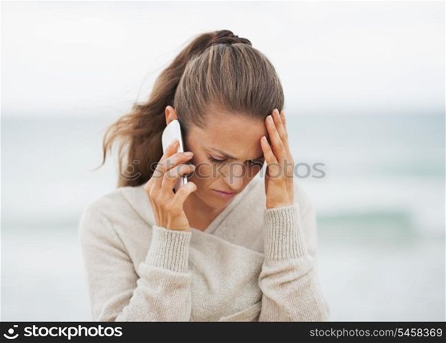 Frustrated young woman in sweater on beach talking cell phone