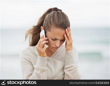 Frustrated young woman in sweater on beach talking cell phone