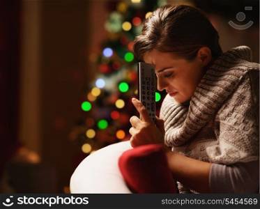 Frustrated young woman with tv remote control in front of christmas tree