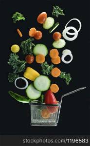 Fry basket with assorted fresh vegetables flying in the air isolated on a dark background. Healthy and vegan food concept.