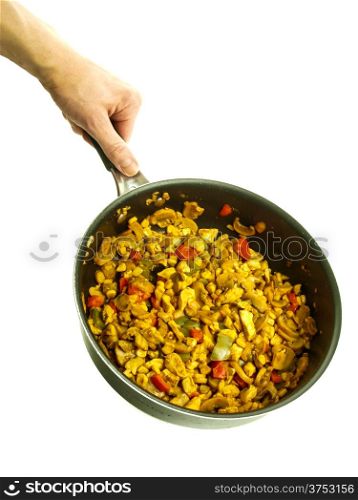 Fry pan with chicken with curry, red pepper and corn held by a male chef towards white background