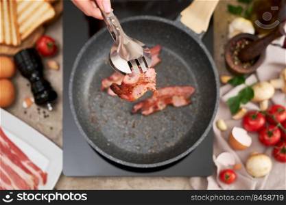 Frying bacon on a pan on induction hob at domestic kitchen.. Frying bacon on a pan on induction hob at domestic kitchen