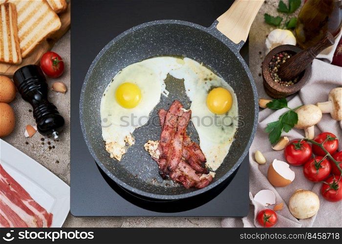 Frying eggs and bacon on a pan on induction hob at domestic kitchen.. Frying eggs and bacon on a pan on induction hob at domestic kitchen