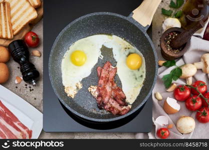 Frying eggs and bacon on a pan on induction hob at domestic kitchen.. Frying eggs and bacon on a pan on induction hob at domestic kitchen