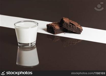 Fudgy chocolate brownies on white background and glass of milk on brown background. Duotone image of brownies and milk. Chocolate dessert and milk.