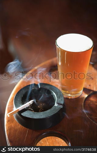 Full beer glass and cigarette with smoke rising in nightclub.