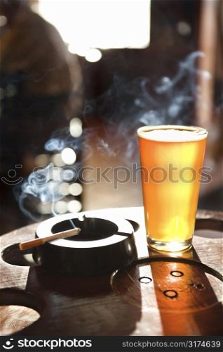 Full beer glass and cigarette with smoke rising in nightclub.