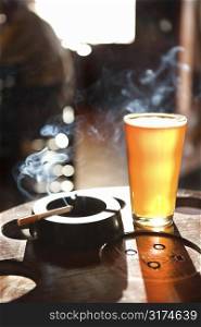 Full beer glass and cigarette with smoke rising in nightclub.